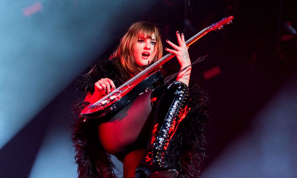 Victoria De Angelis lifts her leg up to perform with her guitar at the 02 arena.