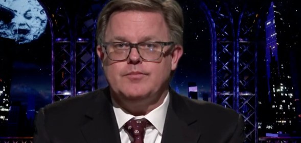 The Good Trouble Show presenter Matt Ford wears a suit and tie against a dark background