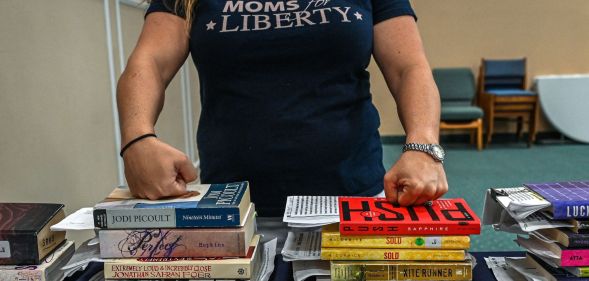 A member of Moms for Liberty rests her knuckles on the tops of a stack of books.