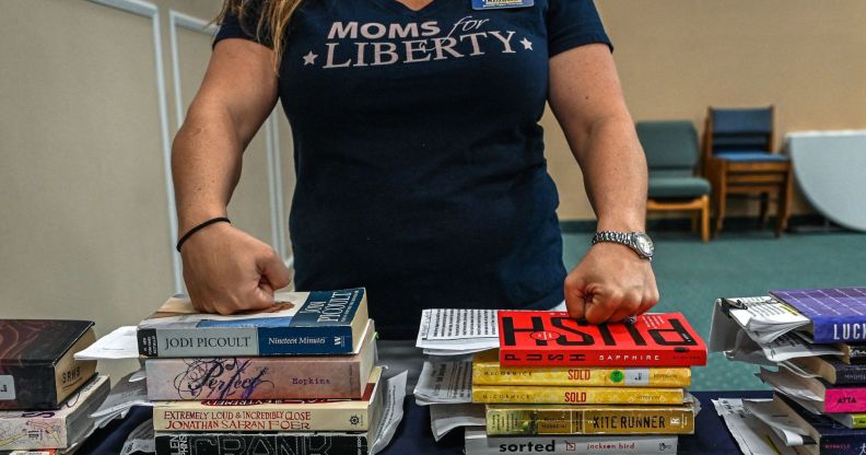 A member of Moms for Liberty rests her knuckles on the tops of a stack of books.