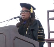 Oprah Winfrey stands behind a podium and microphone wearing a graduation outfit