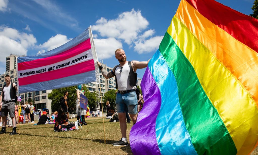 LGBTQ+ activists waving a trans flag and a Pride flag.