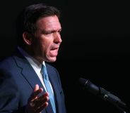 Ron DeSantis, in a blue tie and navy blue suit, speaks infront of a black background.