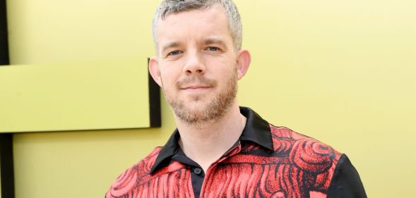 Russell Tovey wearing a black and white shirt while standing in front of a yellow background.