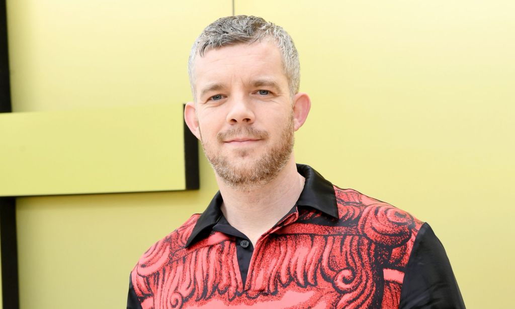 Russell Tovey wearing a black and white shirt while standing in front of a yellow background.