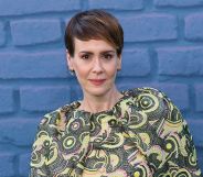 Sarah Paulson wears a patterned green, white and pink top while standing against a blue brick background.