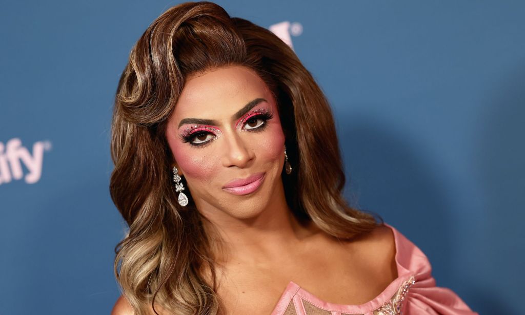 Shangela from the neck up, smiling at the camera, wearing a brown wig and pink make-up.