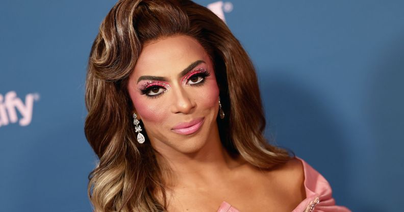 Shangela from the neck up, smiling at the camera, wearing a brown wig and pink make-up.