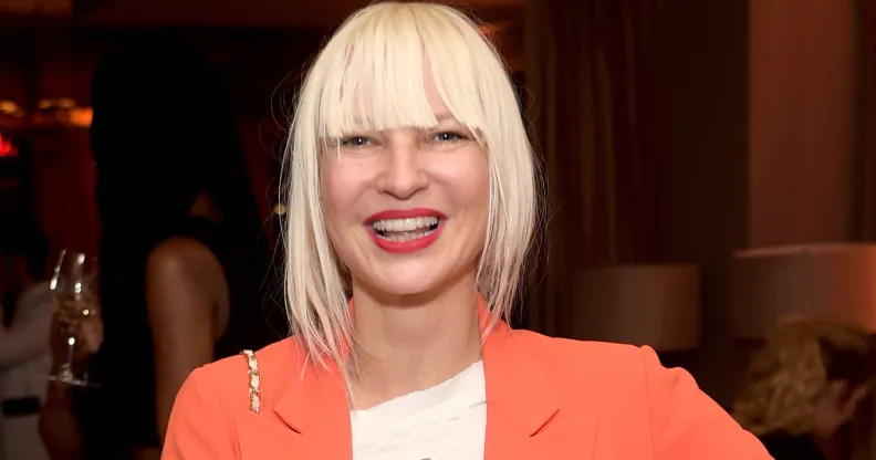 Singer Sia with blonde bangs, an orange jacket and a white top.
