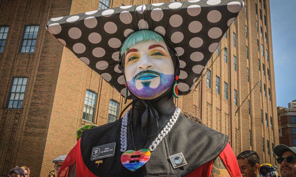 A member of the Sisters of Perpetual Indulgence, wearing an extravagant nun-style costume, glitter beard, and white face paint.