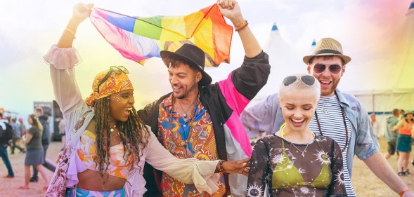 A group of friends at a music festival holding a rainbow Pride flag above their heads
