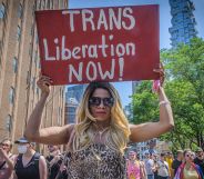 An individual at an LGBTQ+ Pride parade holds a sign of trans solidarity.
