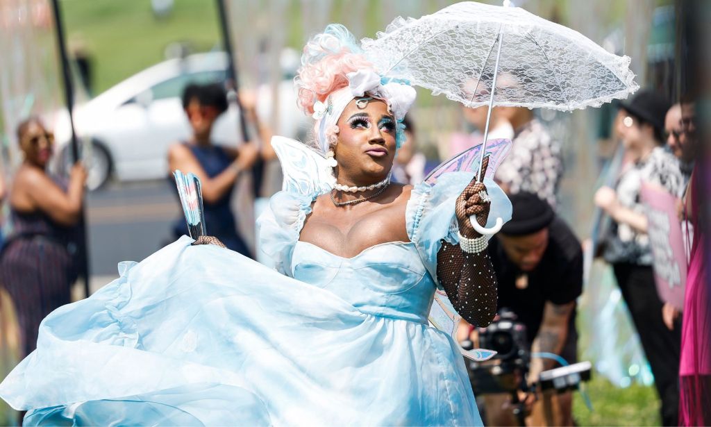 A transgender prom attendee, wearing a blue dress, holds a lace umbrella up.