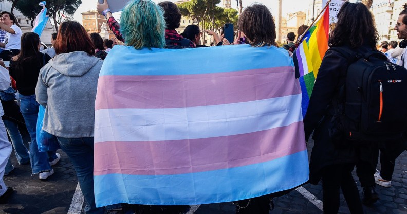 Two people walk away from the camera draped in a trans flag