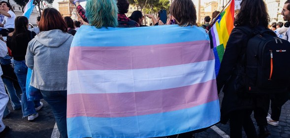 Two people walk away from the camera draped in a trans flag