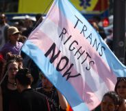 A person holds a giant trans flag that reads 'trans rights now'