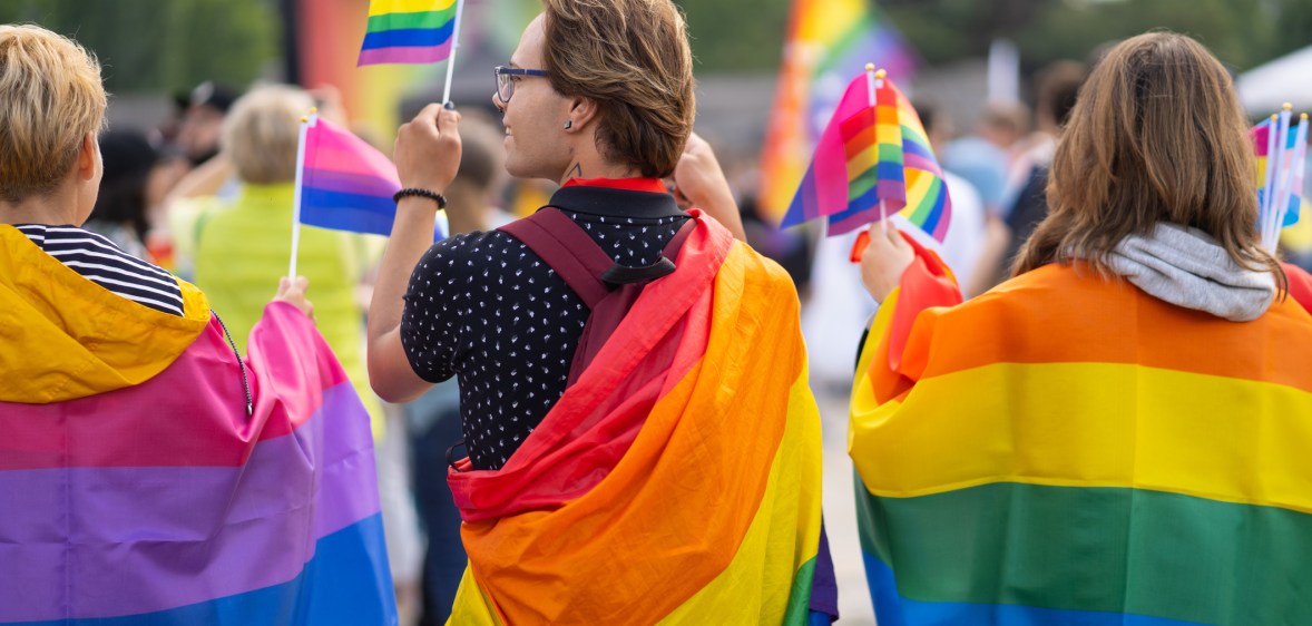 Wrapped in bisexual flag and pride flags this trio are watching a gay pride event