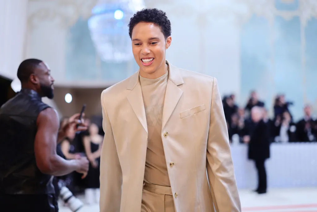 Brittney Griner, a Black woman with short hair, wearing a cream coloured suit on the Met Gala white carpet