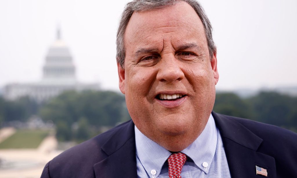 Chris Christie, who is running to be the Republican nominee in the 2024 US presidential race, wears a blue shirt, red tie and dark suit jacket as he smiles at the camera