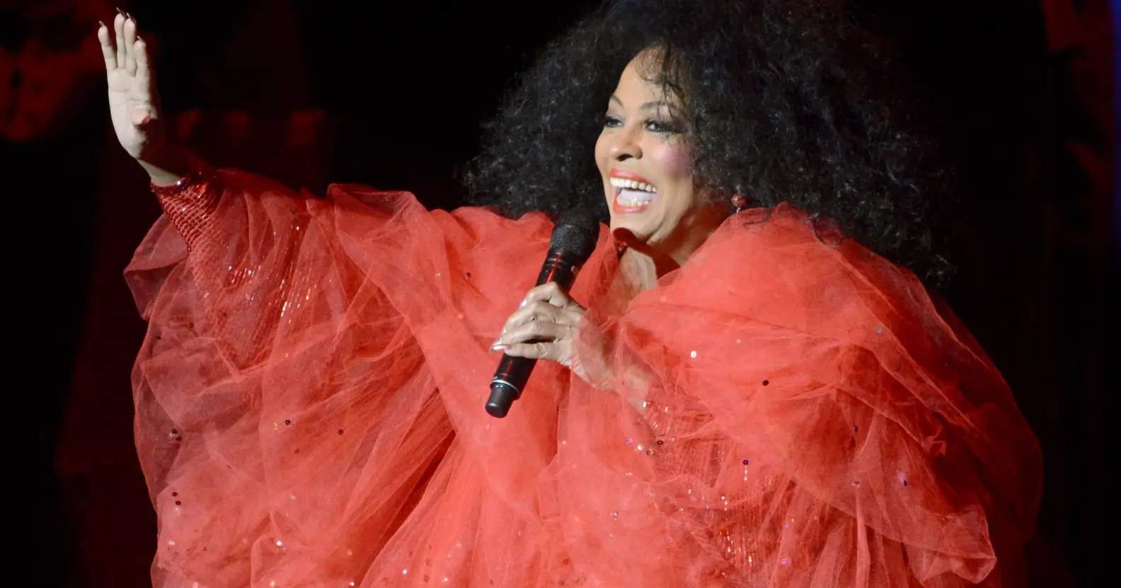 Diana Ross in a red dress performing on stage in concert.