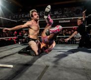 Gay wrestler EFFY kneels in the wrestling ring as he fights his opponent, who has been flipped upside down