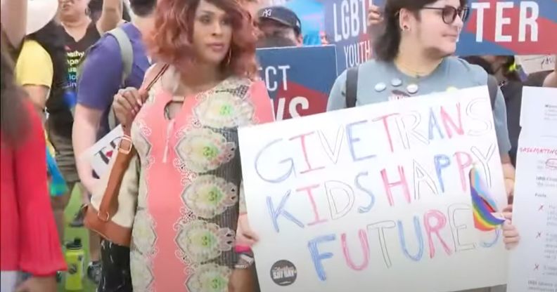 Two people stand amid a protect in Florida holding up a sign reading 'give trans kids happy futures' as the state rolls back access to gender-affirming healthcare for trans youth