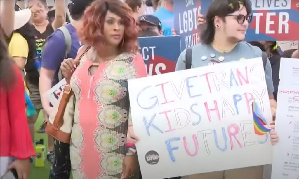 Two people stand amid a protect in Florida holding up a sign reading 'give trans kids happy futures' as the state rolls back access to gender-affirming healthcare for trans youth