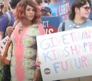 Two people stand amid a protect in Florida holding up a sign reading 'give trans kids happy futures' as the state rolls back access to gender-affirming healthcare for trans youth