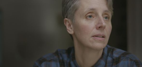 A still of anti-trans campaigner Kathleen Stock wearing a blue plaid shirt as she looks off screen from the Channel 4 documentary Gender Wars