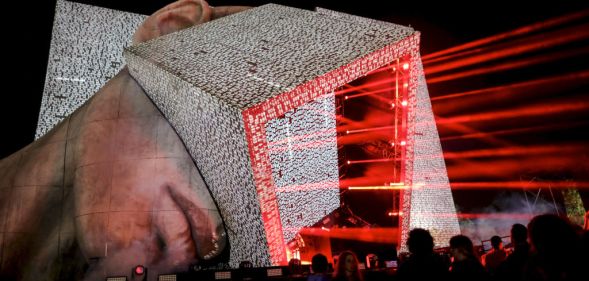 A huge festival stage in the shape of a human head with a cube protruding from it