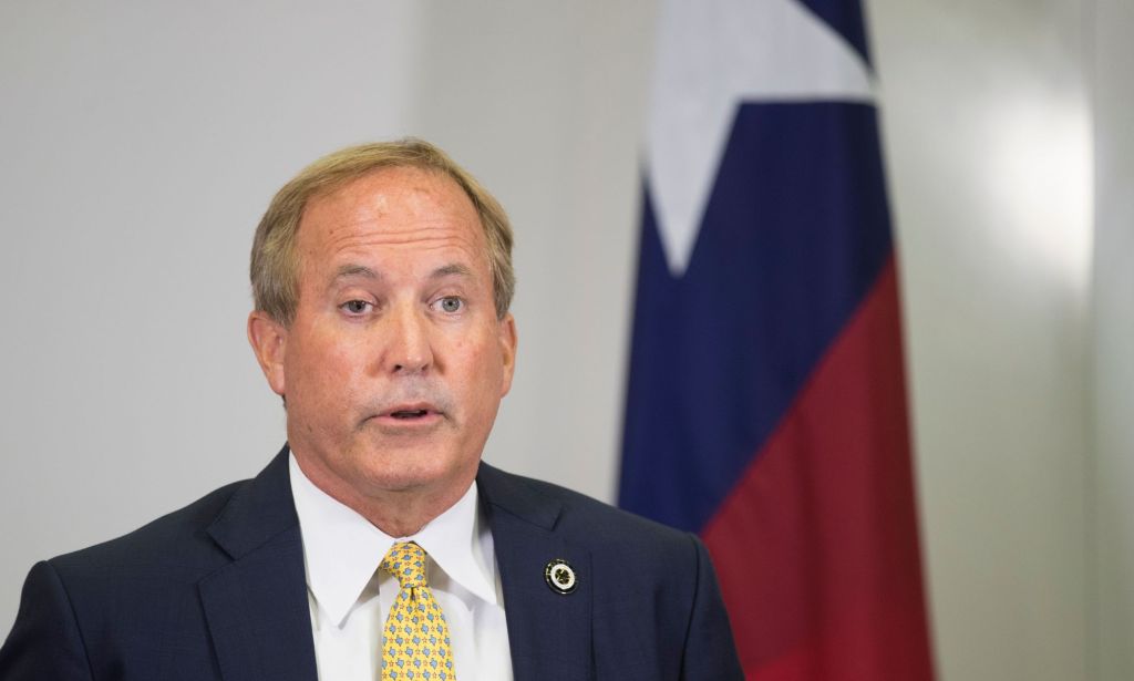 Texas attorney general Ken Paxton, who has repeatedly pushed back on trans rights in the states, speaks to people off camera while wearing a white shirt, yellow tie and dark suit jacket