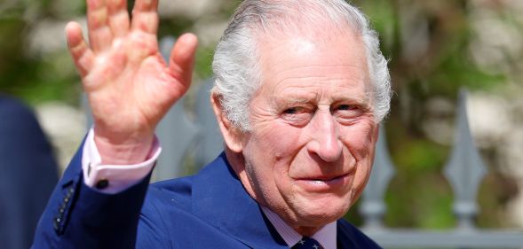 King Charles III wears a blue suit as he waves at people gathered outside