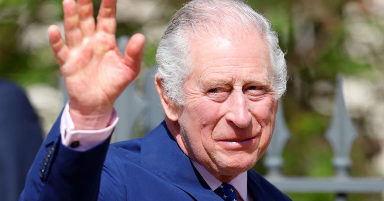King Charles III wears a blue suit as he waves at people gathered outside