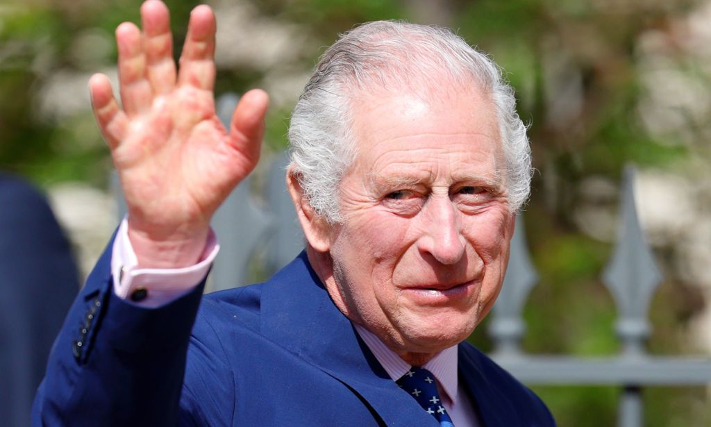 King Charles III wears a blue suit as he waves at people gathered outside