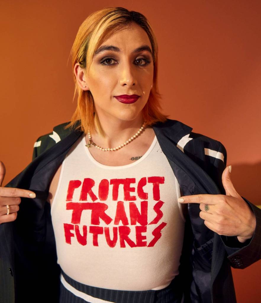 Non-binary actor Mason Alexander Park wears a shirt reading 'Protect trans futures' with a black jacket