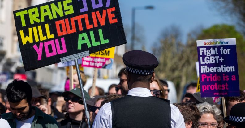 A person holds up a sign reading 'Trans joy will outlive you all' in support of the LGBTQ+ community and a drag event at the Honor Oak Pub as the individual stands in front of a Met Police officer