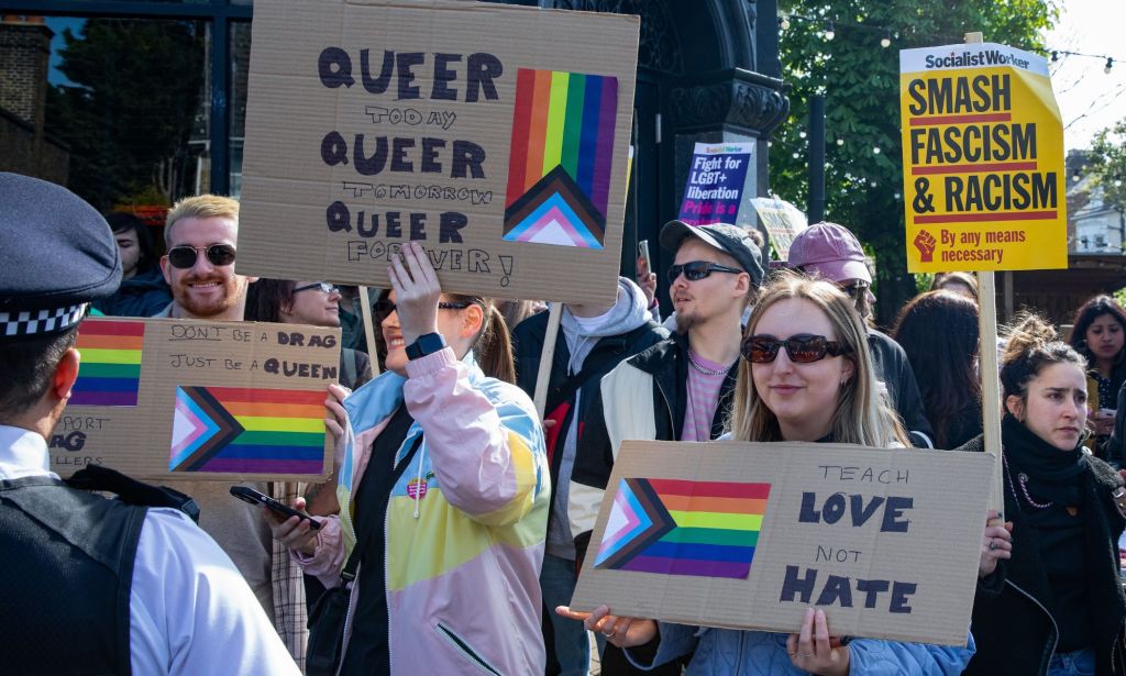 People hold up signs in support of the LGBTQ+ community and a drag event in front of a Met Police officer in London