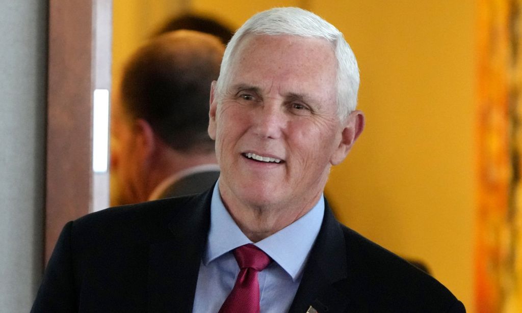 Mike Pence, who is thought to be a potential 2024 Republican presidential candidate, wears a blue shirt, red tie and dark jacket as he smiles to someone off camera