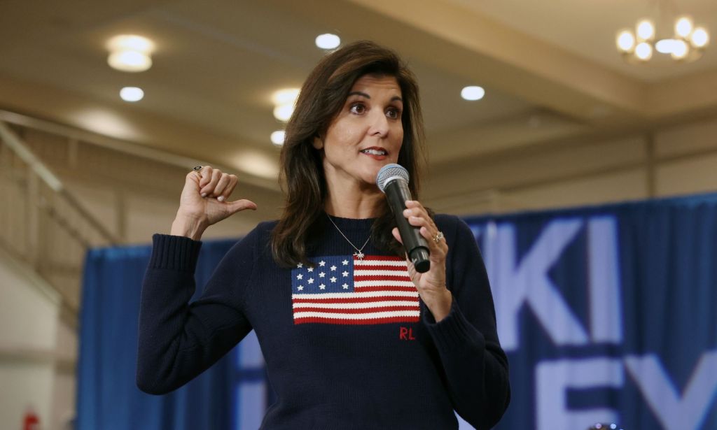 Nikki Haley, a Republican candidate for the 2024 presidential campaign, wears a black shirt with a US flag on it as she gestures to somewhere behind her and speaks into a microphone