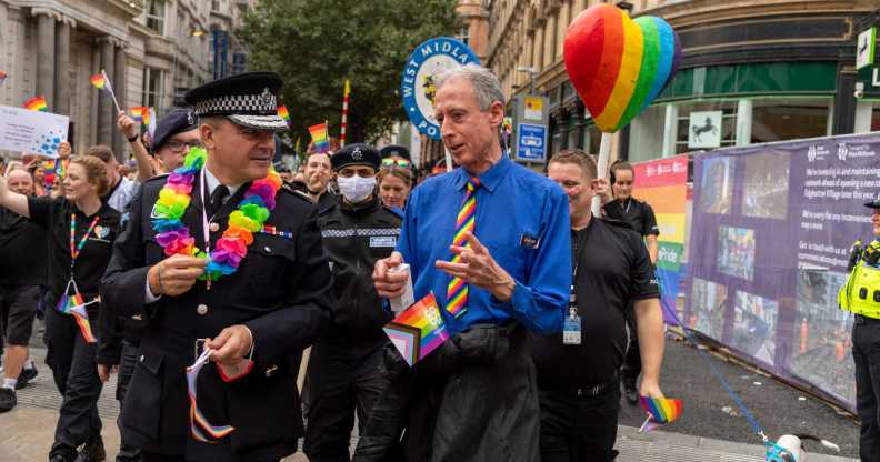 Peter Tatchell talking to the West Midlands Police chief while walking in a Pride march, surrounded by police holding rainbow flags