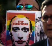 A person holds up a sign with the face of Russia's president Vladimir Putin with an LGBTQ+ rainbow flag in the background and words 'stop homophobia' on it as Putin's government increasingly attacks queer people and labels LGBTQ+ rights groups as 'foreign agents'