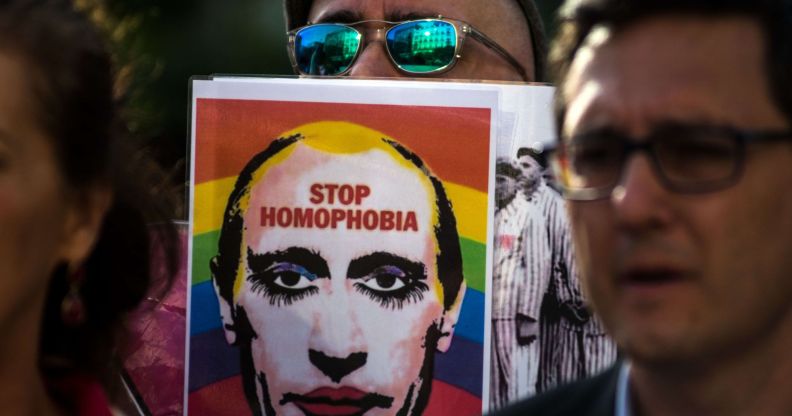 A person holds up a sign with the face of Russia's president Vladimir Putin with an LGBTQ+ rainbow flag in the background and words 'stop homophobia' on it as Putin's government increasingly attacks queer people and labels LGBTQ+ rights groups as 'foreign agents'