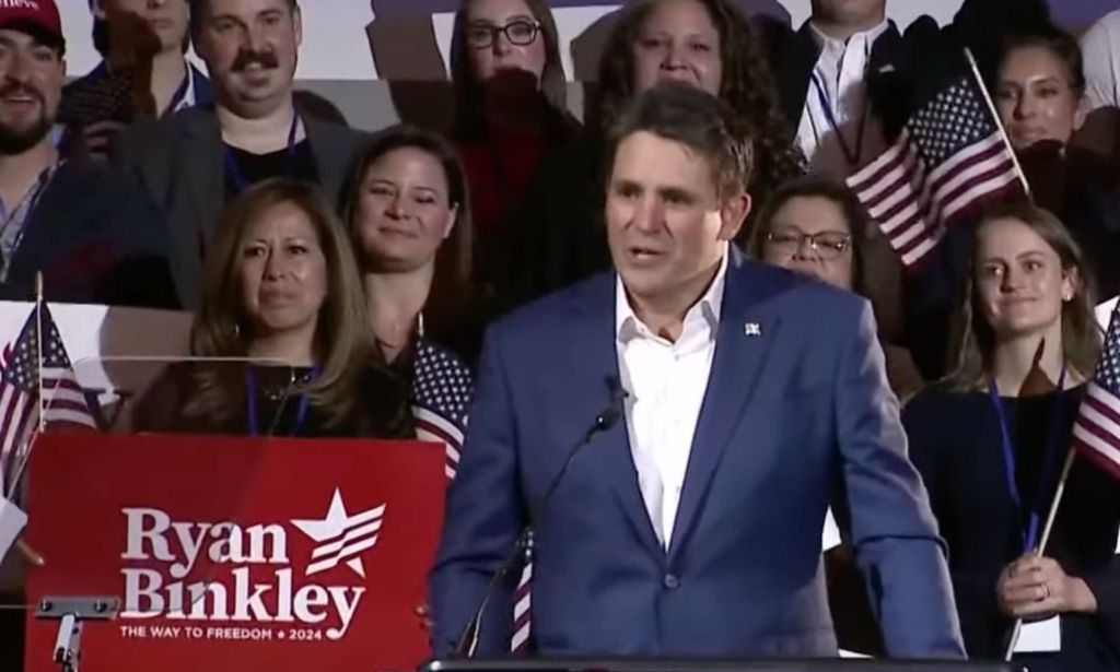 Ryan Binkley, who is a 2024 Republican presidential candidate, wears a white shirt and blue jacket as he speaks at a rally