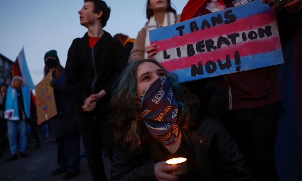 A person holds up a sign reading 'trans liberation now' in the blue, pink and white colours of the trans pride flag