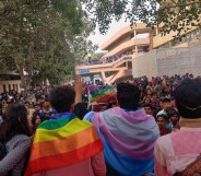 A group of Indian marchers at a Pride Parade, one draped in a transgender flag, the other in a pride flag.