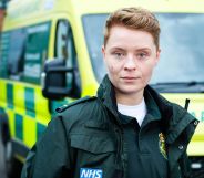 Actor Arin Smethurst as Casualty character Sah. Sah wears a green paramedic's outfit and stands against a UK ambulance.