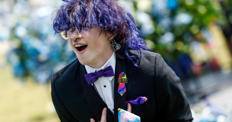An Arkansas queer young person, wearing a suit and bow tie, leans over with their hands pointing inward.