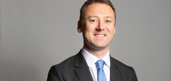 Conservative MP Brendan Clarke-Smith standing in a suit and blue tie against a grey background