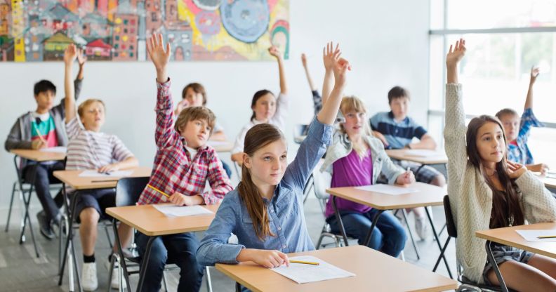 Children sit in a classroom holding their hands up