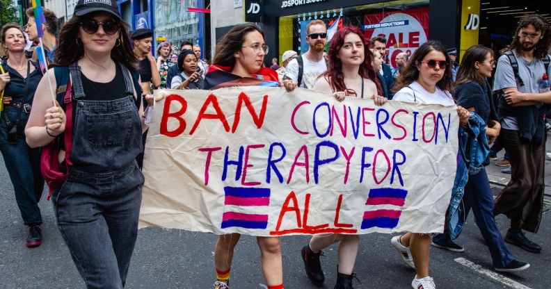 Activists hold a sign reading "ban conversion therapy for all."